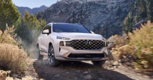 A white 2022 Hyundai Santa Fe being driven in a wooded area with a mountain in the background. | Hyundai dealer in Little Rock, AR.