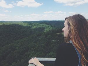 A woman standing high on a balcony looking down at the landscape full of lush green trees. | Things to do in Little Rock, AR.