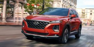 Red 2019 Hyundai Santa Fe Sport being driven on the highway with buildings in the background. | Hyundai dealer in Little Rock, AR.