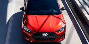 Close view of the front of an reddish-orange 2020 Hyundai Veloster with the headlights on being driven on the highway.| Hyundai dealer in Little Rock, AR.