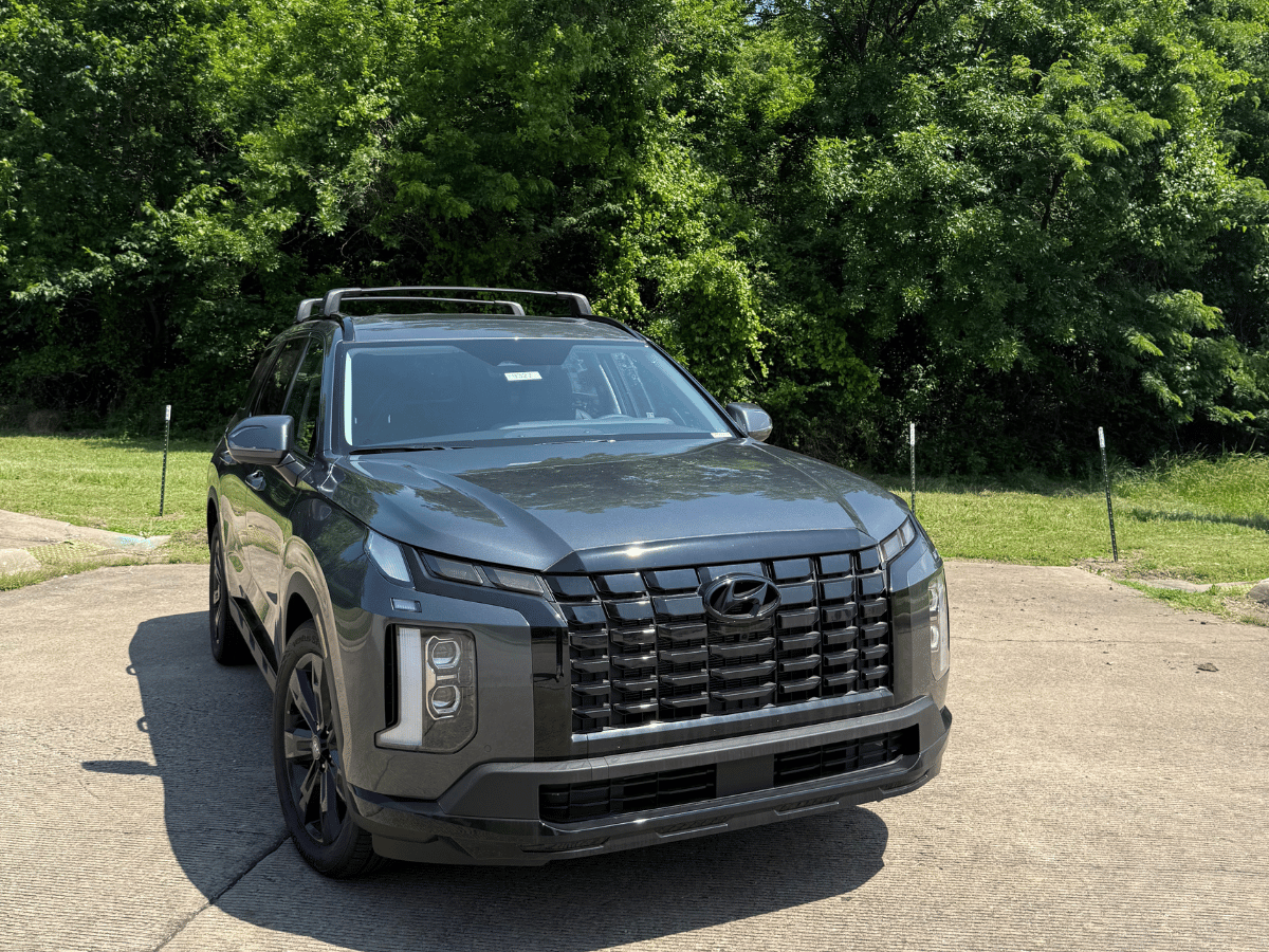 2025 Hyundai Palisade in a dark gray finish parked on pavement near green trees, highlighting its bold front grille and modern SUV design at Crain Hyundai of Little Rock.
